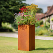 Rust-colored metal planter with flowers in a garden setting